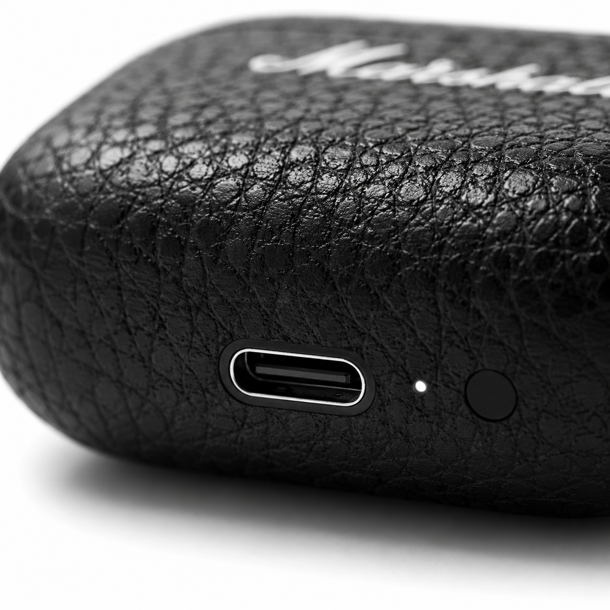 Macro close-up of a premium black true wireless earbuds charging case showing the USB Type-C charging port, LED charging indicator, textured leather-like finish, and minimalist design