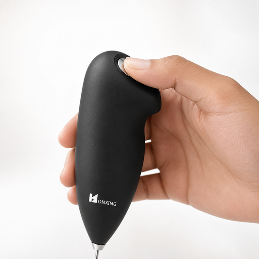 Close-up of a hand pressing the one-touch power button on a handheld electric milk frother with ergonomic soft-touch grip, demonstrating simple and comfortable operation for quick milk frothing.