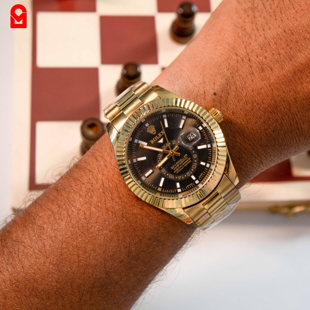 Gold tone automatic watch worn on wrist showing black dial, date window and gold bracelet.