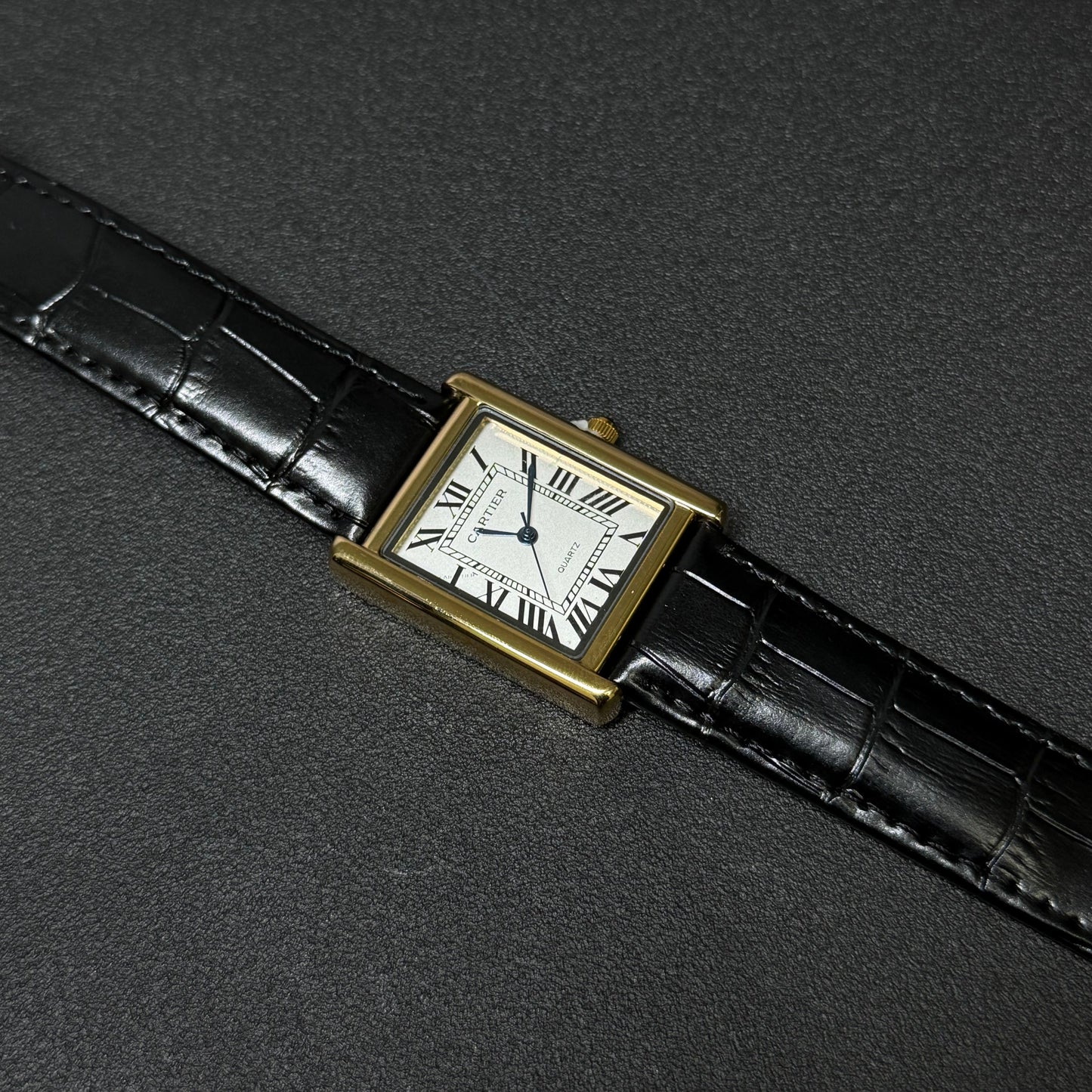 Vintage watch with black leather strap and gold case on a dark gray background