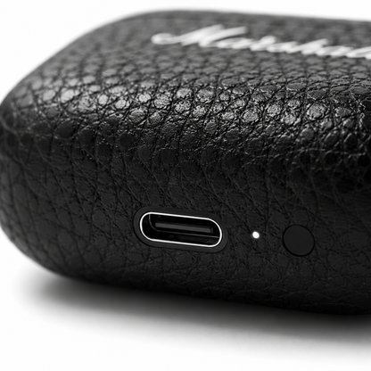Macro close-up of a premium black true wireless earbuds charging case showing the USB Type-C charging port, LED charging indicator, textured leather-like finish, and minimalist design