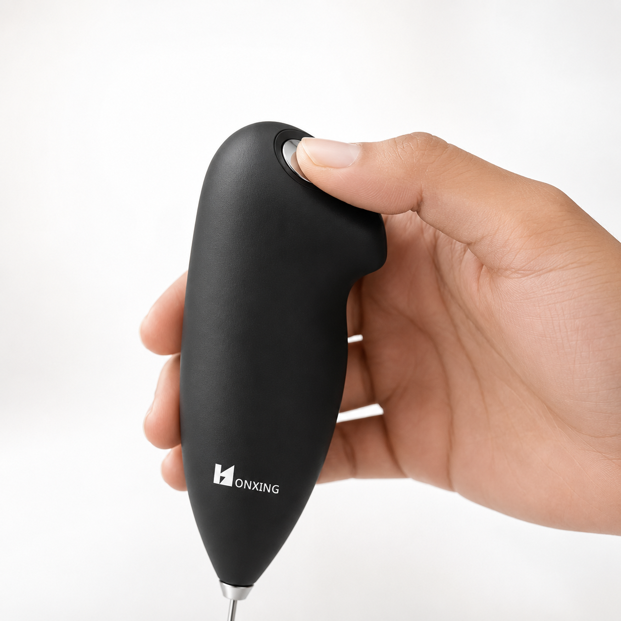 Close-up of a hand pressing the one-touch power button on a handheld electric milk frother with ergonomic soft-touch grip, demonstrating simple and comfortable operation for quick milk frothing.