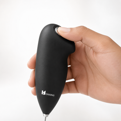 Close-up of a hand pressing the one-touch power button on a handheld electric milk frother with ergonomic soft-touch grip, demonstrating simple and comfortable operation for quick milk frothing.