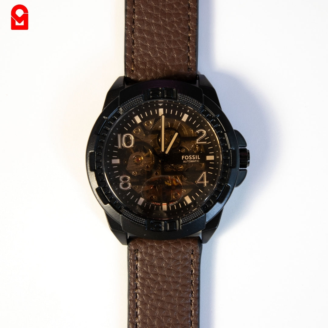 Close-up view of black automatic skeleton dial watch showing visible mechanical movement and brown leather strap.