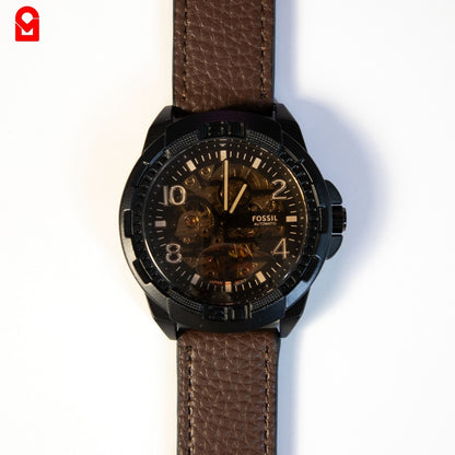 Close-up view of black automatic skeleton dial watch showing visible mechanical movement and brown leather strap.