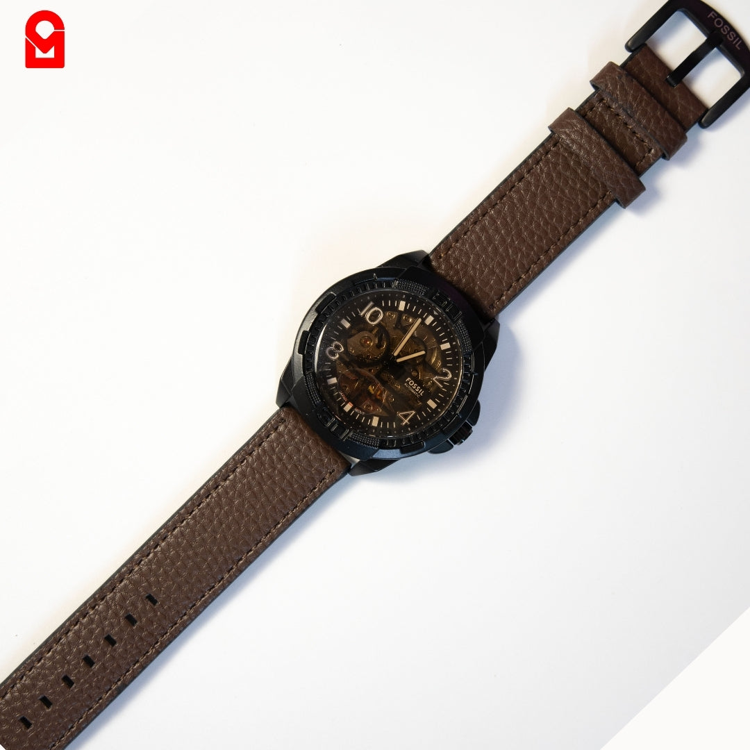 Black automatic skeleton watch with brown leather strap displayed on white background.