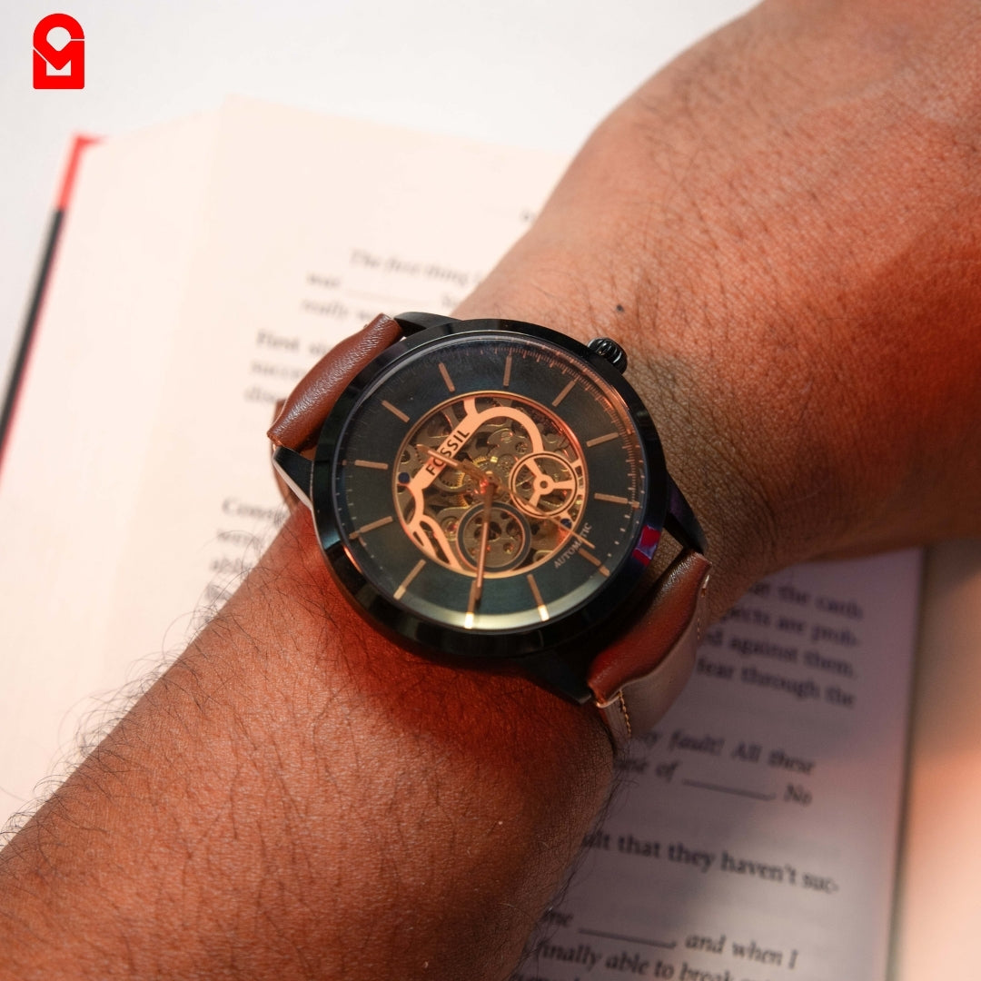 Black skeleton automatic watch worn on wrist with brown leather strap.