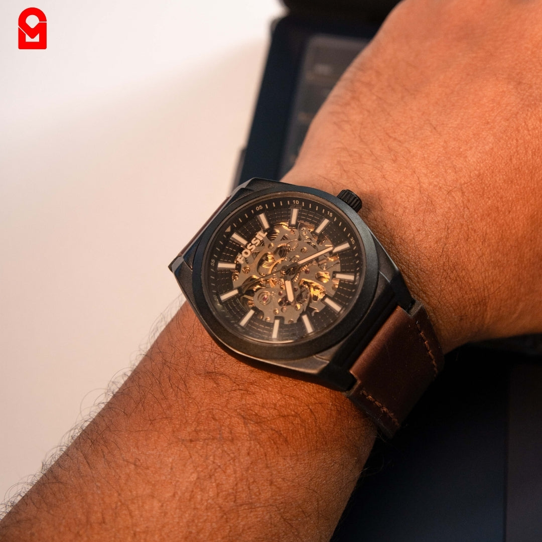 Black automatic skeleton watch worn on wrist with brown leather strap.
