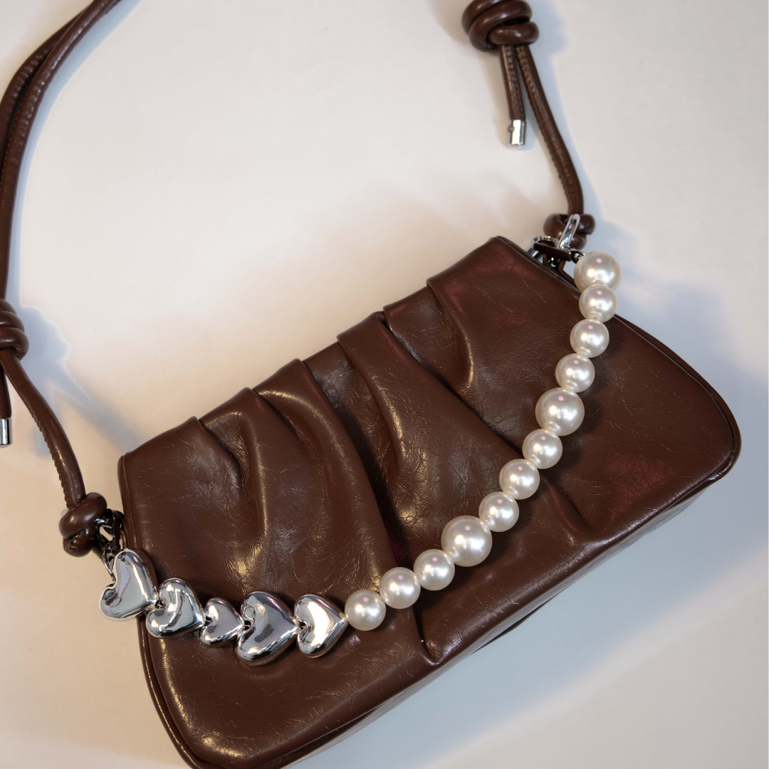Brown shoulder bag featuring pearl chain and adjustable strap.