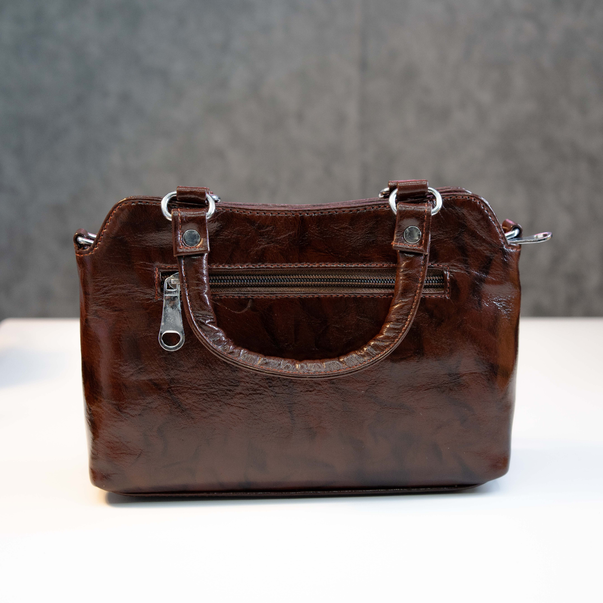 Brown leather top handle bag showing back zip pocket and smooth finish.