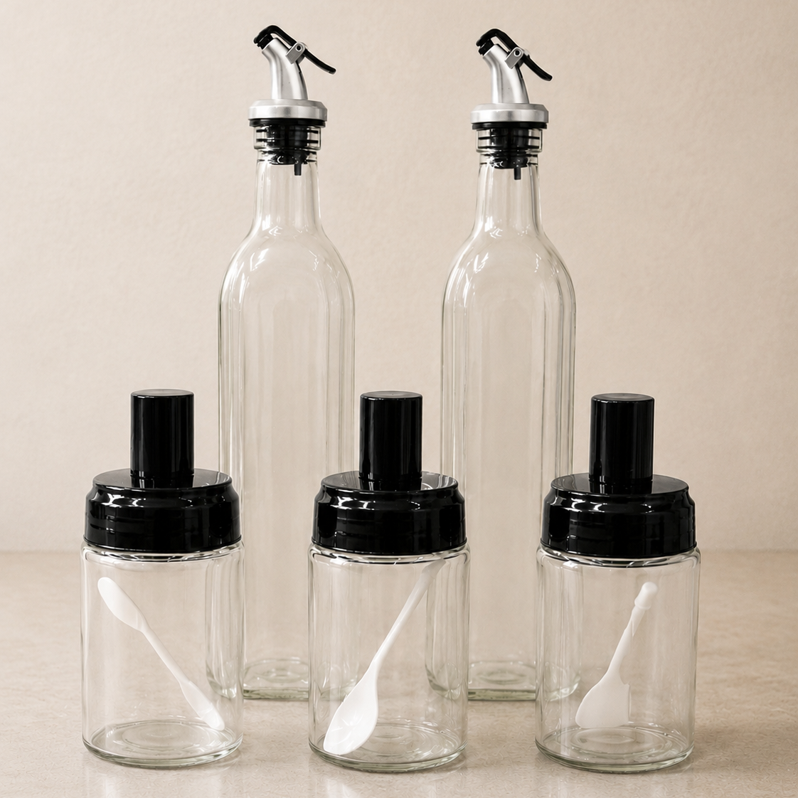 Glass Oil Dispenser & Spice Container Set with 2 glass oil bottles, 3 spice jars and built-in measuring spoons on a neutral kitchen background