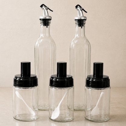 Glass Oil Dispenser & Spice Container Set with 2 glass oil bottles, 3 spice jars and built-in measuring spoons on a neutral kitchen background