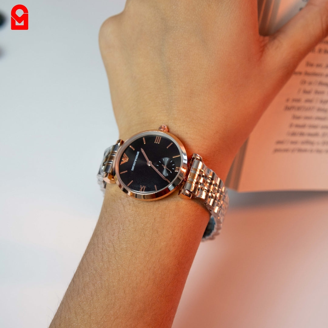 Gold and black automatic women’s watch worn on wrist showing stainless steel bracelet.