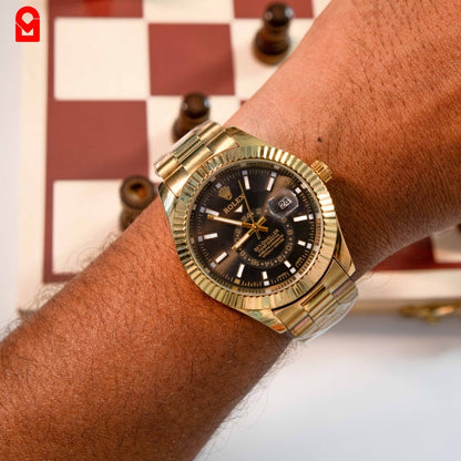 Gold tone automatic watch worn on wrist showing black dial, date window and gold bracelet.