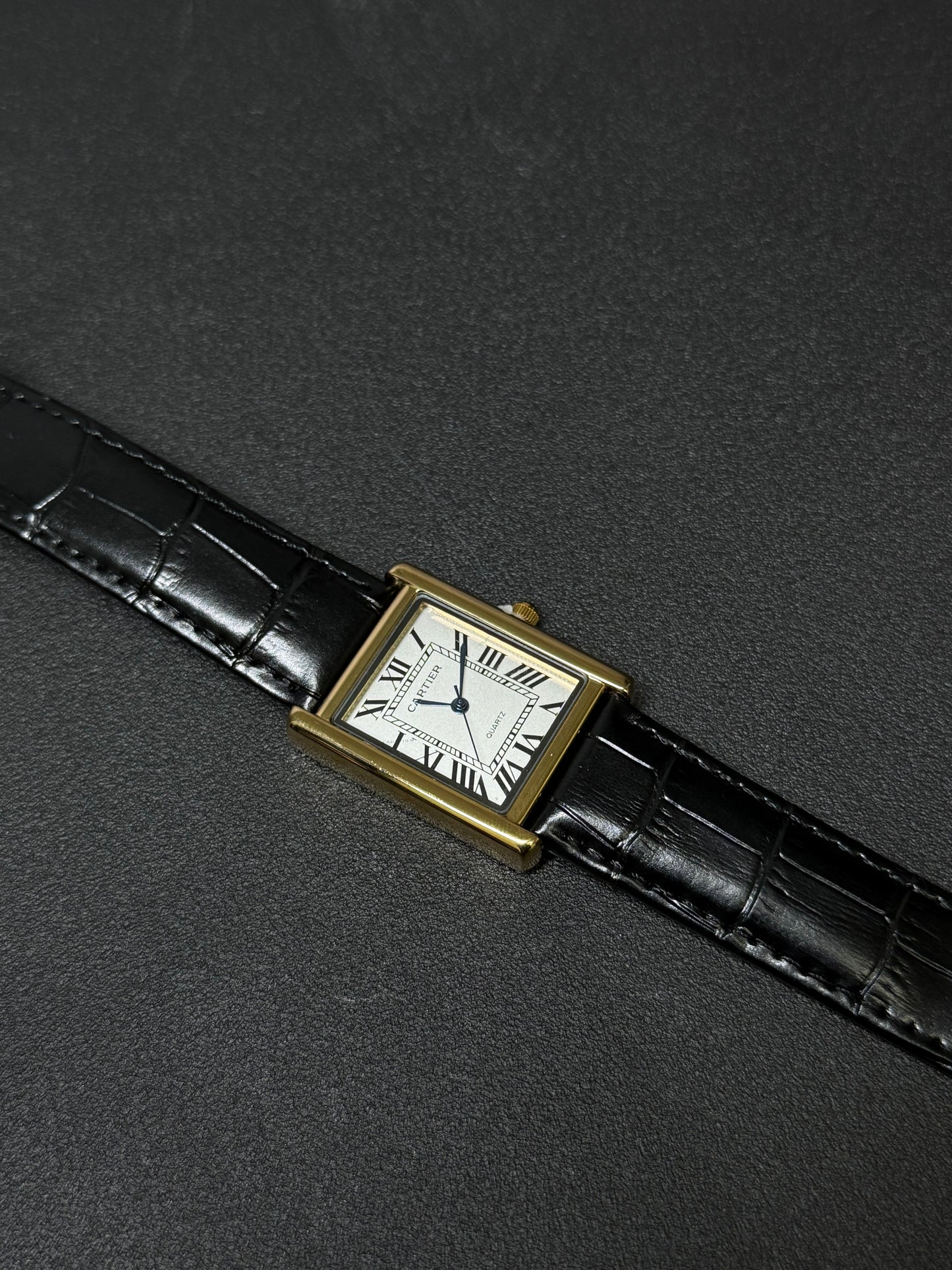 Vintage watch with black leather strap and gold case on a dark gray background