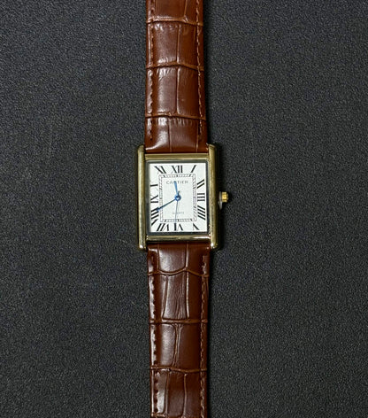 Replica watch featuring brown leather strap, white rectangular dial, Roman numerals and classic gold-tone case design