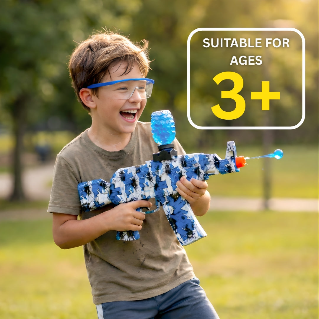 Child holding Kids Electric Gel Blaster Gun Kit with Safety Glasses outdoors, smiling with a vibrant blue gel bead in motion, with text 'SUITABLE FOR AGES 3+'.