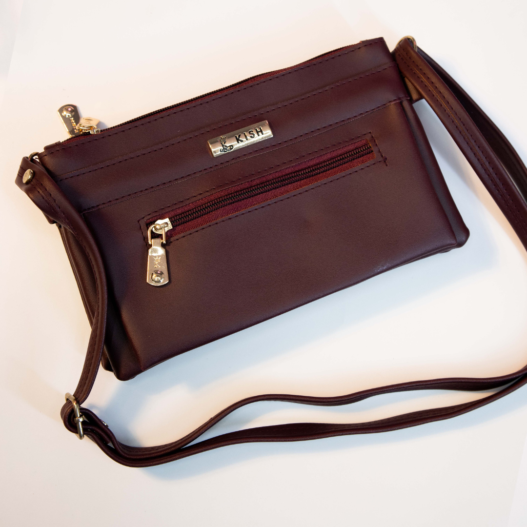 Maroon compact sling bag with front zip pocket and adjustable shoulder strap.