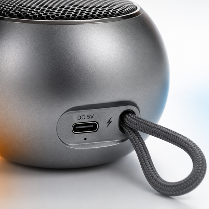 Rear close-up of the portable metal Bluetooth speaker featuring a USB Type-C charging port, LED charging indicator, and integrated braided lanyard for convenient portability.