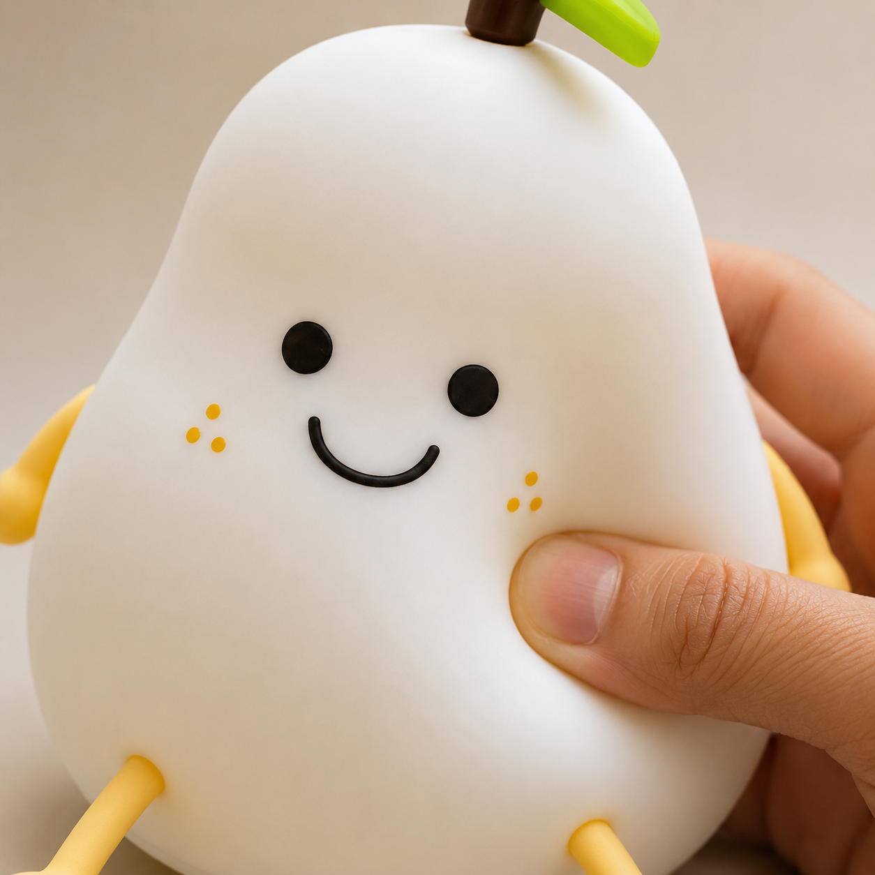 Hand gently pressing soft silicone pear night lamp, demonstrating squishy touch material, cute bedside sleeping light and child-friendly room décor lamp.