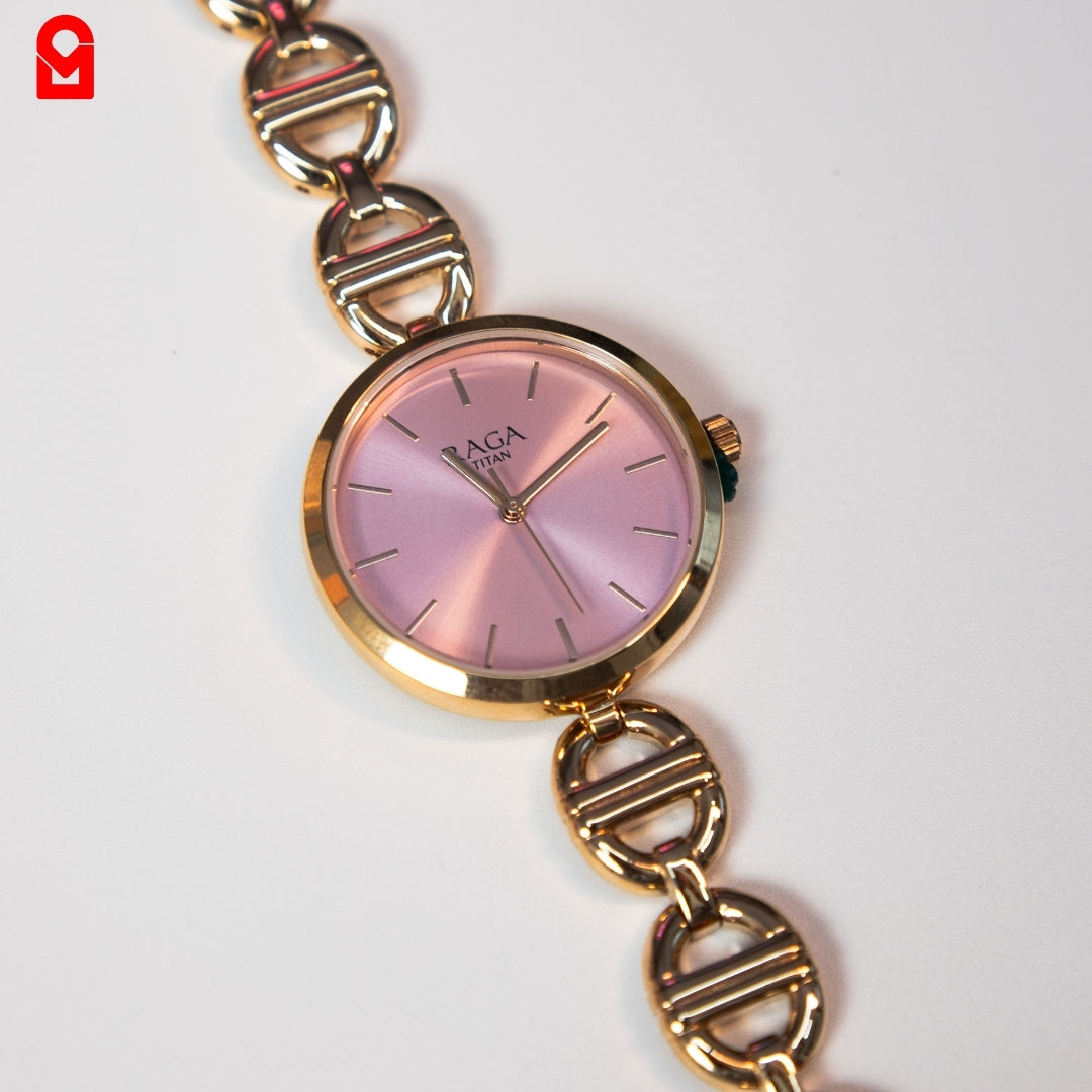 Close-up of women’s pink dial analog watch with gold tone case and bracelet strap.