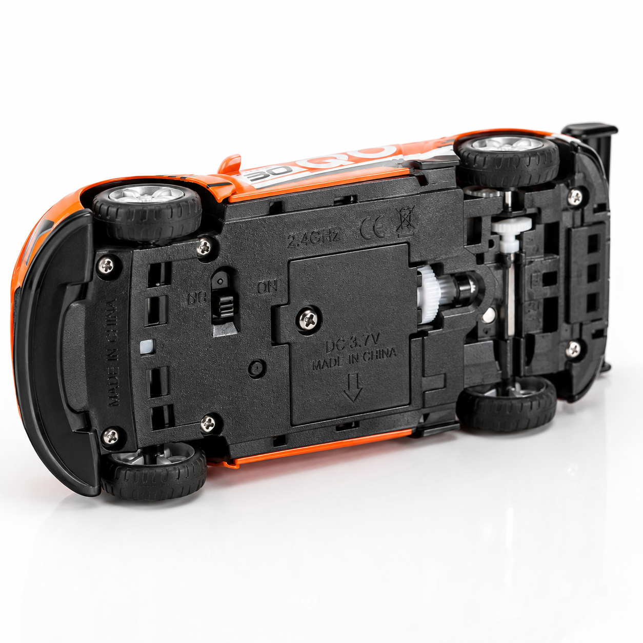 Bottom view of a 1:64 mini RC racing car showing the battery compartment, 2.4GHz wireless system, on/off switch, durable wheels, and alloy chassis construction.