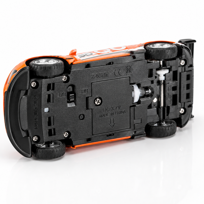 Bottom view of a 1:64 mini RC racing car showing the battery compartment, 2.4GHz wireless system, on/off switch, durable wheels, and alloy chassis construction.