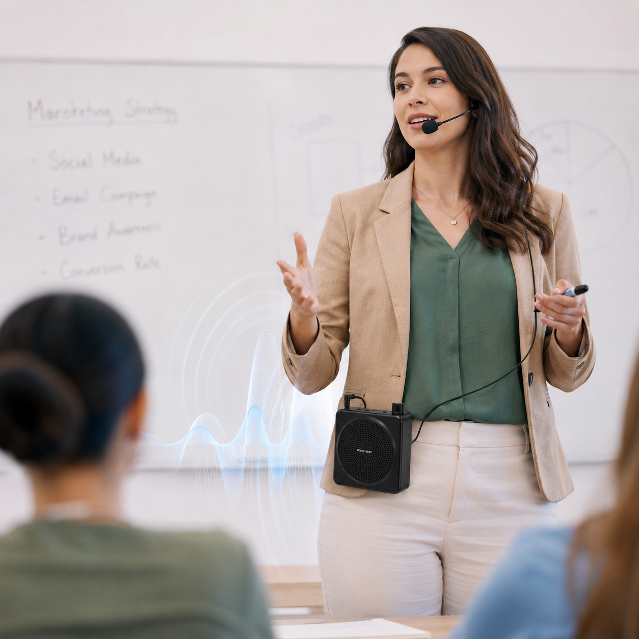 Female teacher wearing a headset microphone and portable voice amplifier during a classroom presentation, demonstrating hands-free voice amplification for lectures, training sessions, and public speaking.