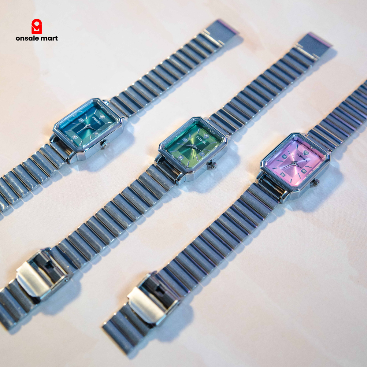 Multiple rectangular steel watches with stainless steel expansion bracelets in pink, green, and teal dials.