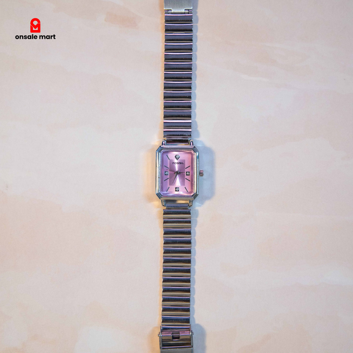 Rectangular steel watch with soft pink dial and crystal-style hour markers.