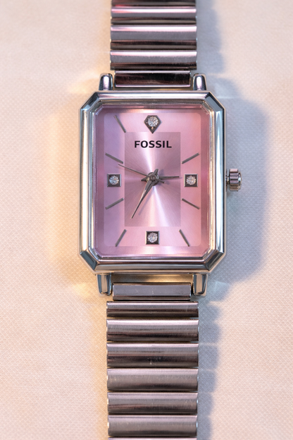 Close-up of rectangular steel watch dial with pink sunburst finish and crystal hour markers.