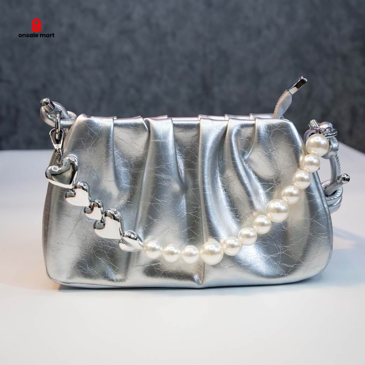 Silver ruched shoulder bag with pearl chain handle on white background.