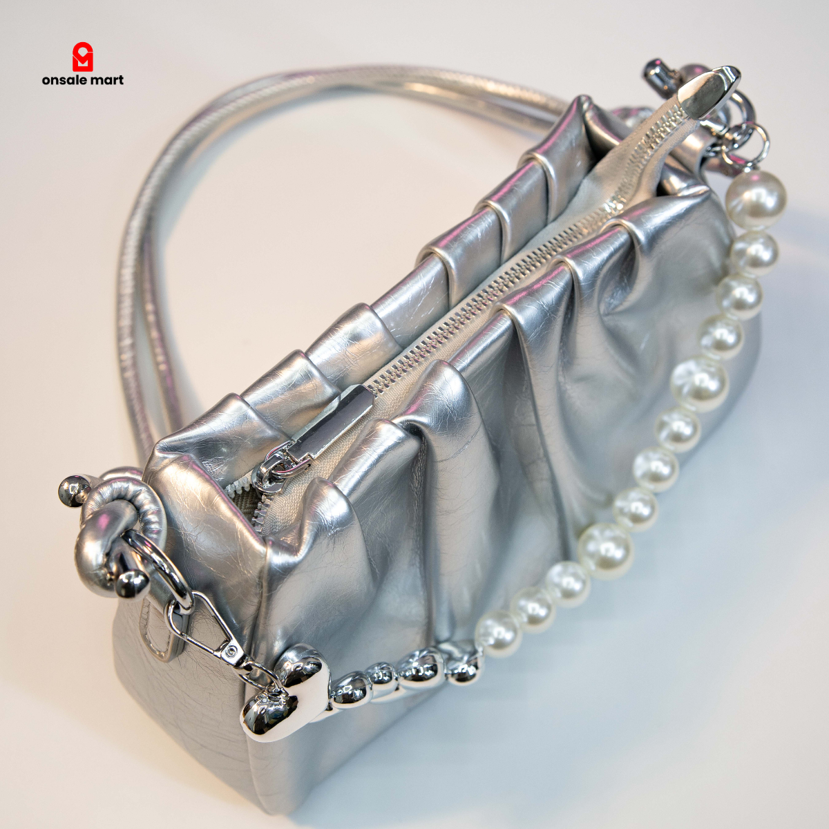 Silver shoulder bag with ruched design and zip closure.