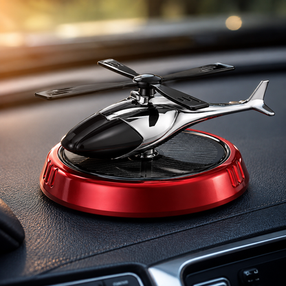 Premium solar helicopter car air freshener displayed on a vehicle dashboard with sunlight illuminating the solar panel. The glossy black helicopter sits on a metallic red base, adding fragrance and decorative appeal to the car interior.