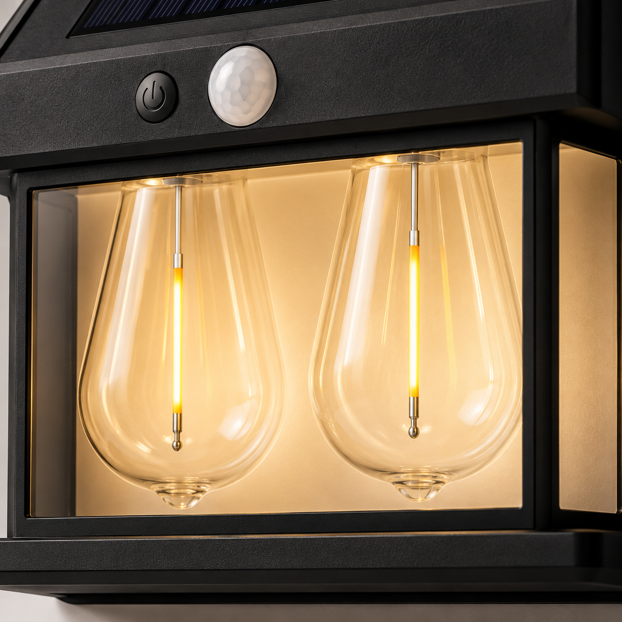 Close-up of the solar wall lamp with two warm white LED filament-style light chambers glowing behind transparent covers, highlighting the PIR motion sensor, premium black housing, and modern outdoor lighting design.