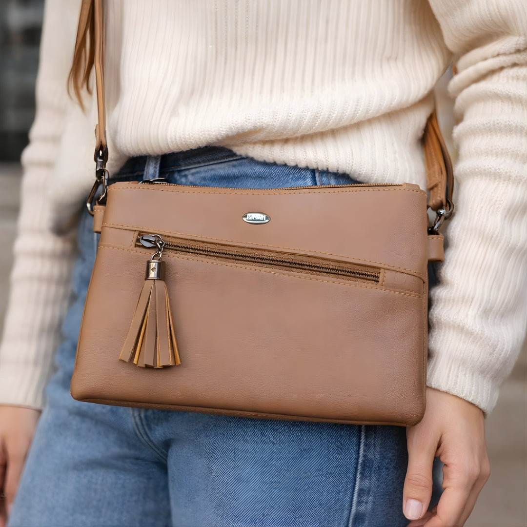 Tan zip closure crossbody sling bag worn with casual outfit.