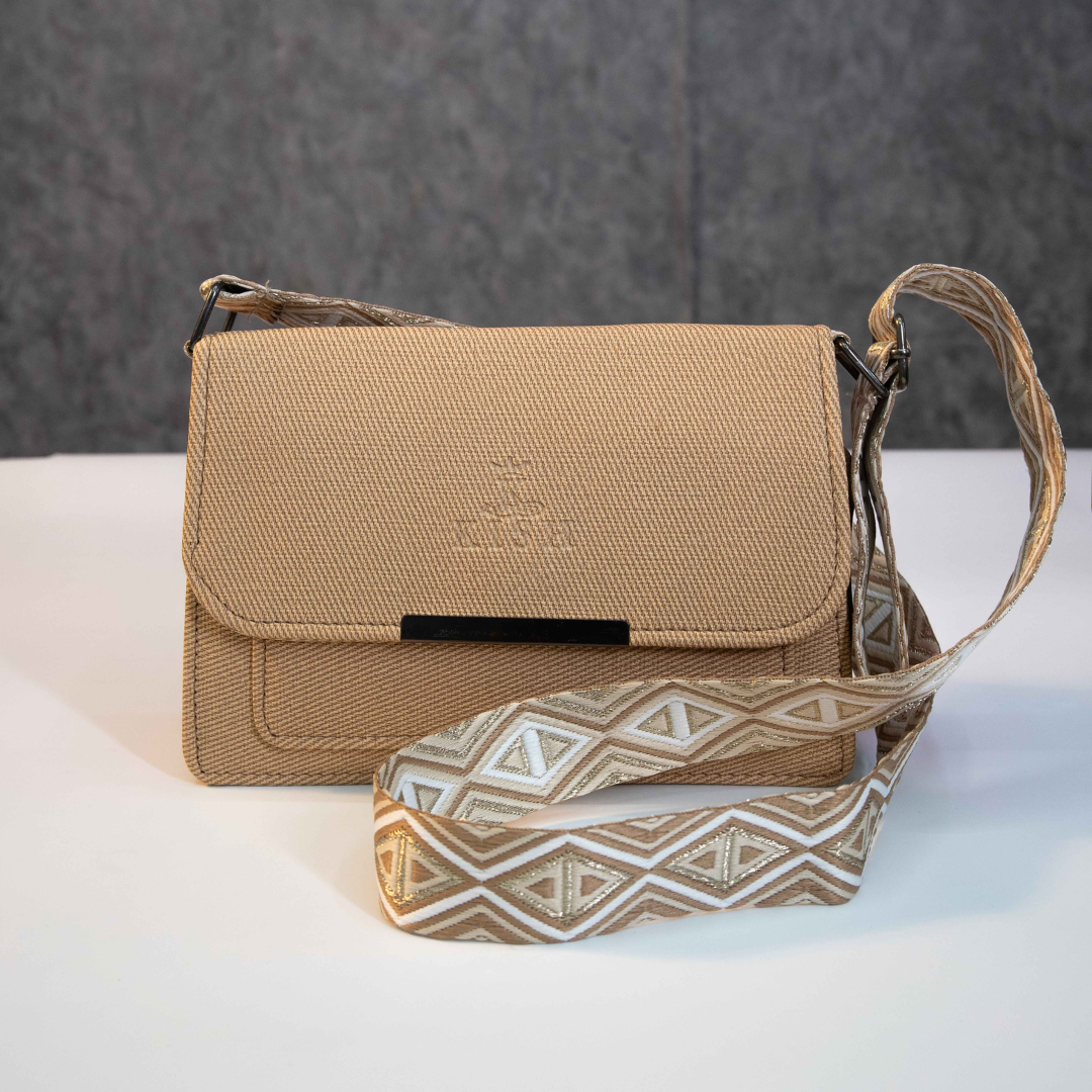 Beige textured sling bag with flap closure and adjustable patterned strap.