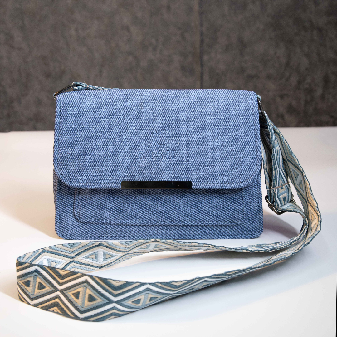 Blue textured crossbody sling bag with flap closure and patterned strap.