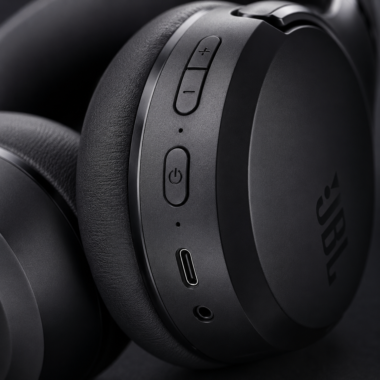 Macro view of JBL Tour One M3 headphone controls featuring power button, volume controls, USB-C charging port, 3.5mm audio jack and integrated microphone.