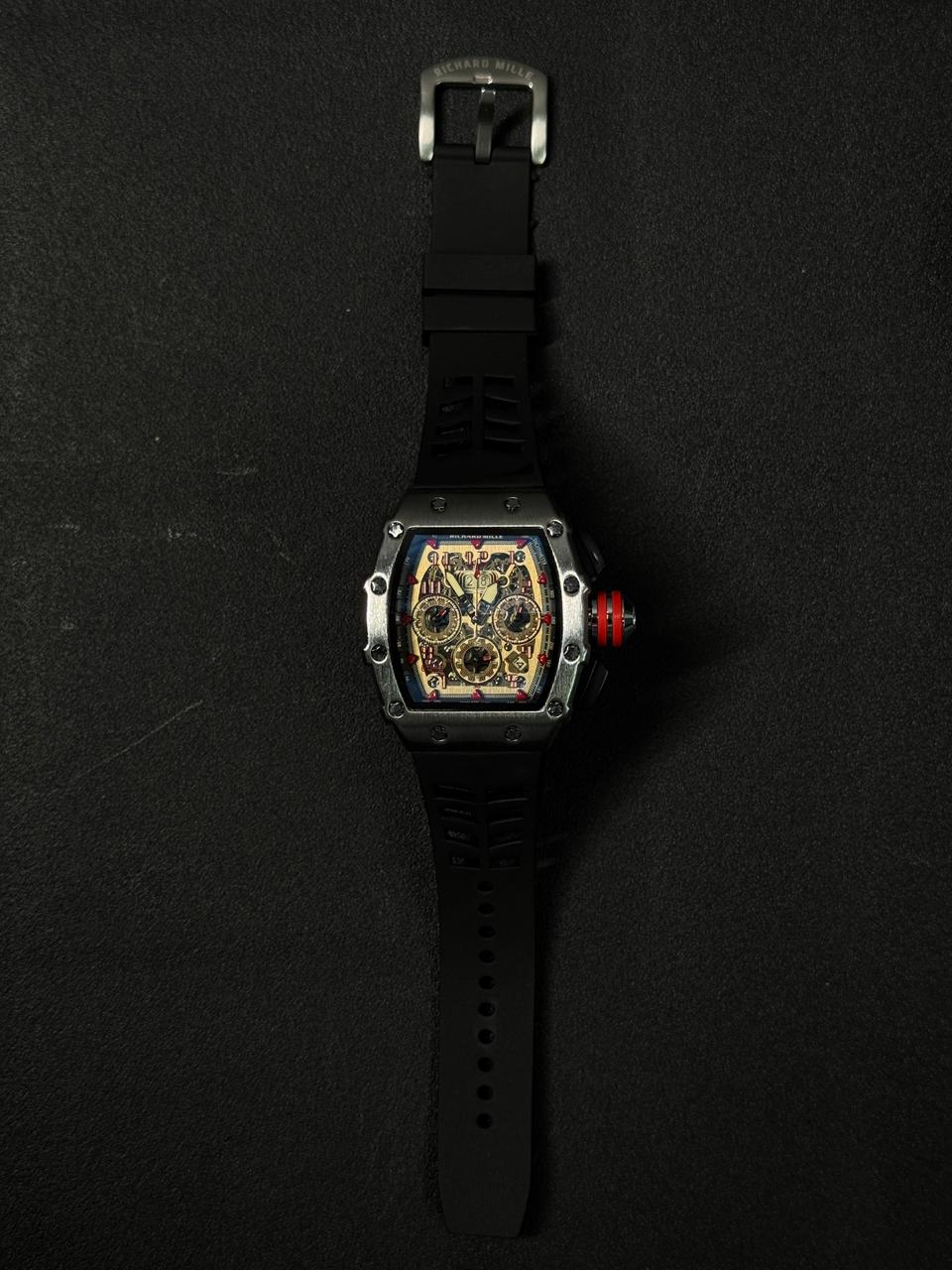 Luxury replica watch with a skeleton dial, a curved industrial silver case, a red-rimmed crown, and a black sports rubber band.