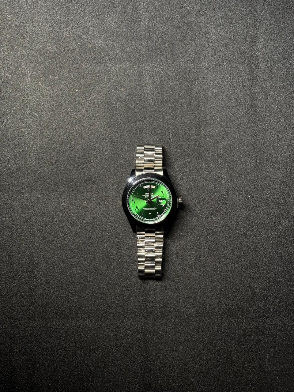 Replica green dial stainless steel watch featuring day date display, silver metal bracelet and premium luxury inspired design on black background