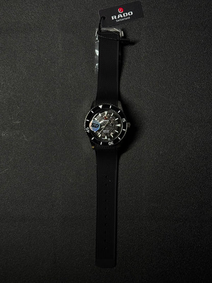 Black replica watch with transparent skeleton dial, black silicone strap, and diver-inspired bezel on a textured black surface.