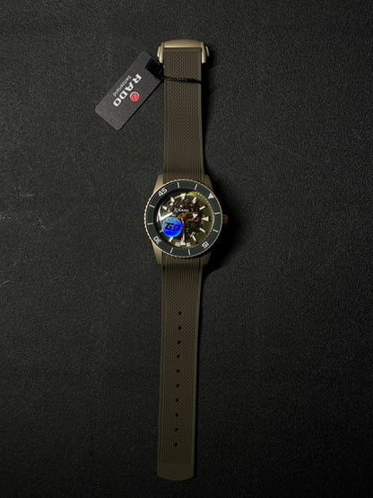 Olive green replica watch with skeleton dial, textured silicone strap, and luxury diver-style bezel displayed on a black background.