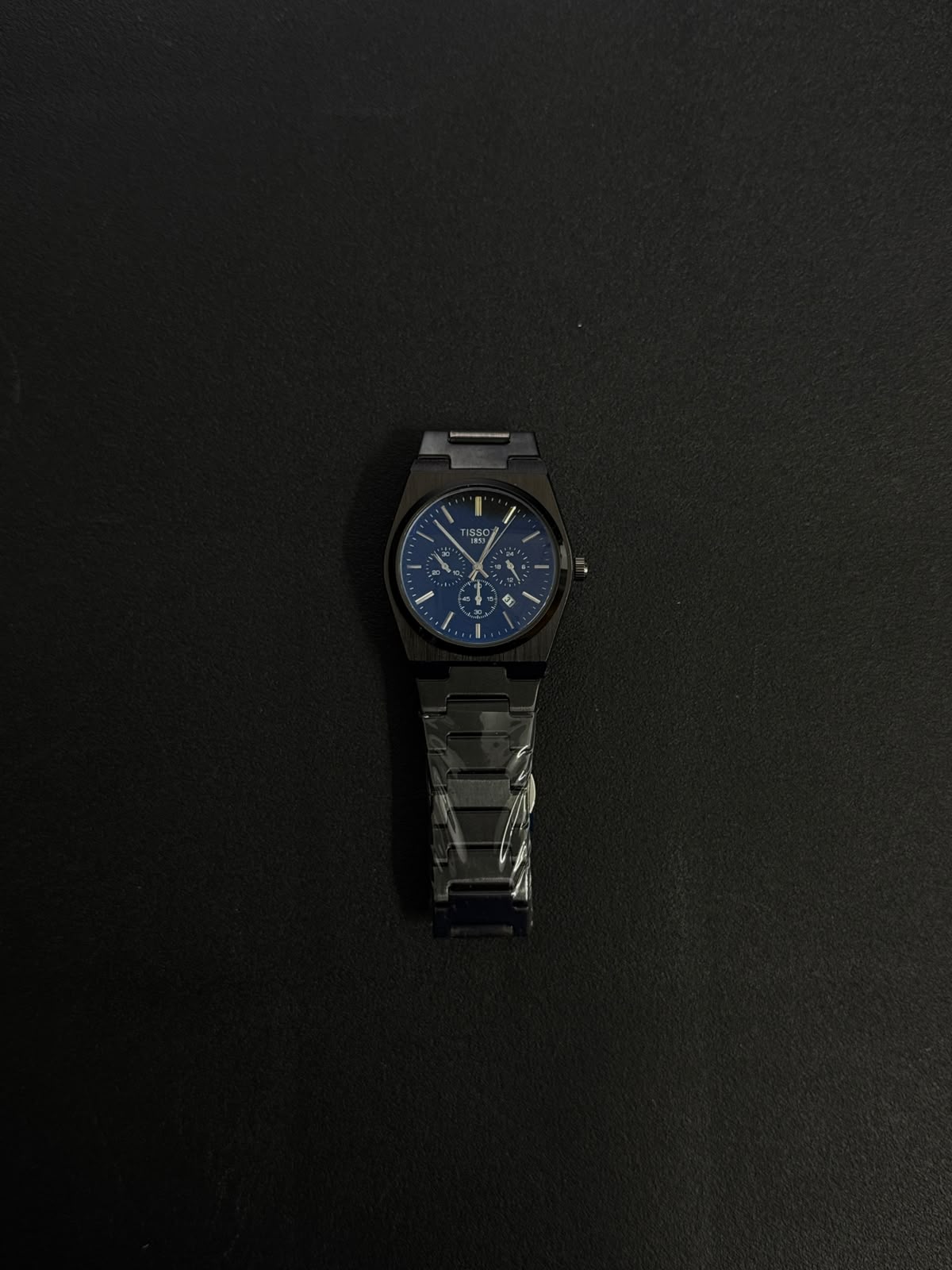 Black replica watch with blue dial, integrated metal bracelet and modern luxury chronograph-inspired styling.