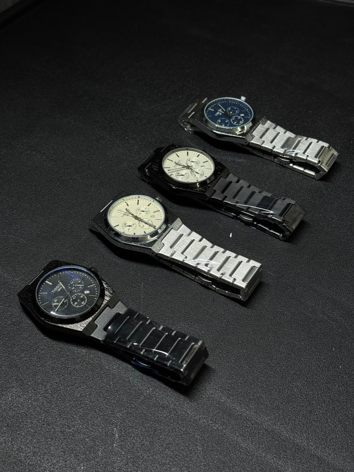Luxury replica watch collection featuring black, blue, silver and white dial variants with integrated stainless steel bracelets on black background.