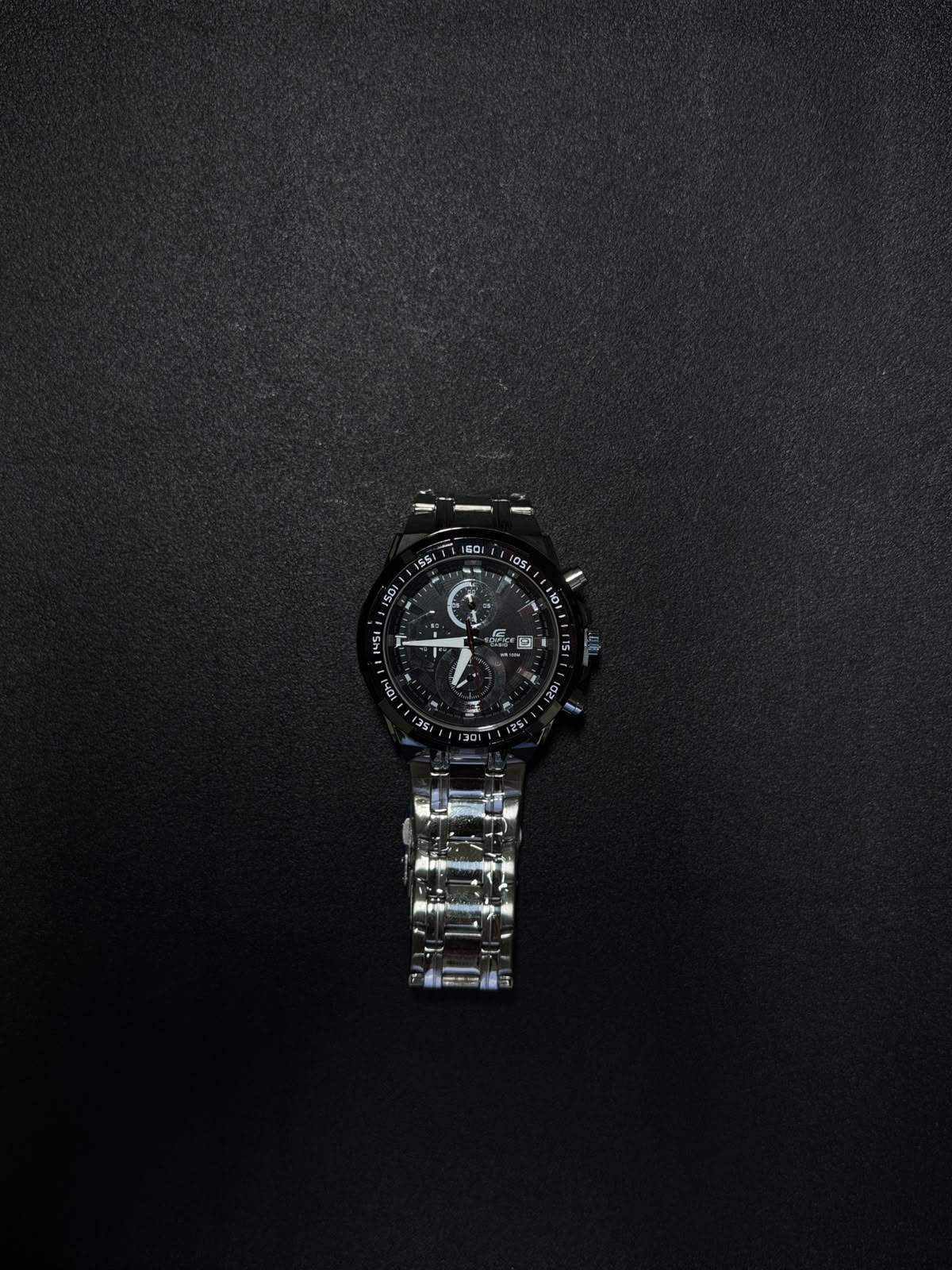 Black stainless steel replica chronograph watch with analog display, date window and luxury sports-inspired design on dark background.