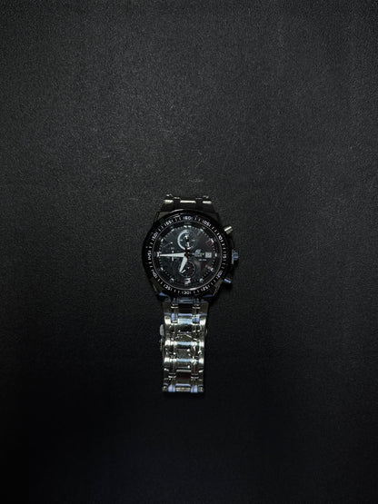 Black stainless steel replica chronograph watch with analog display, date window and luxury sports-inspired design on dark background.