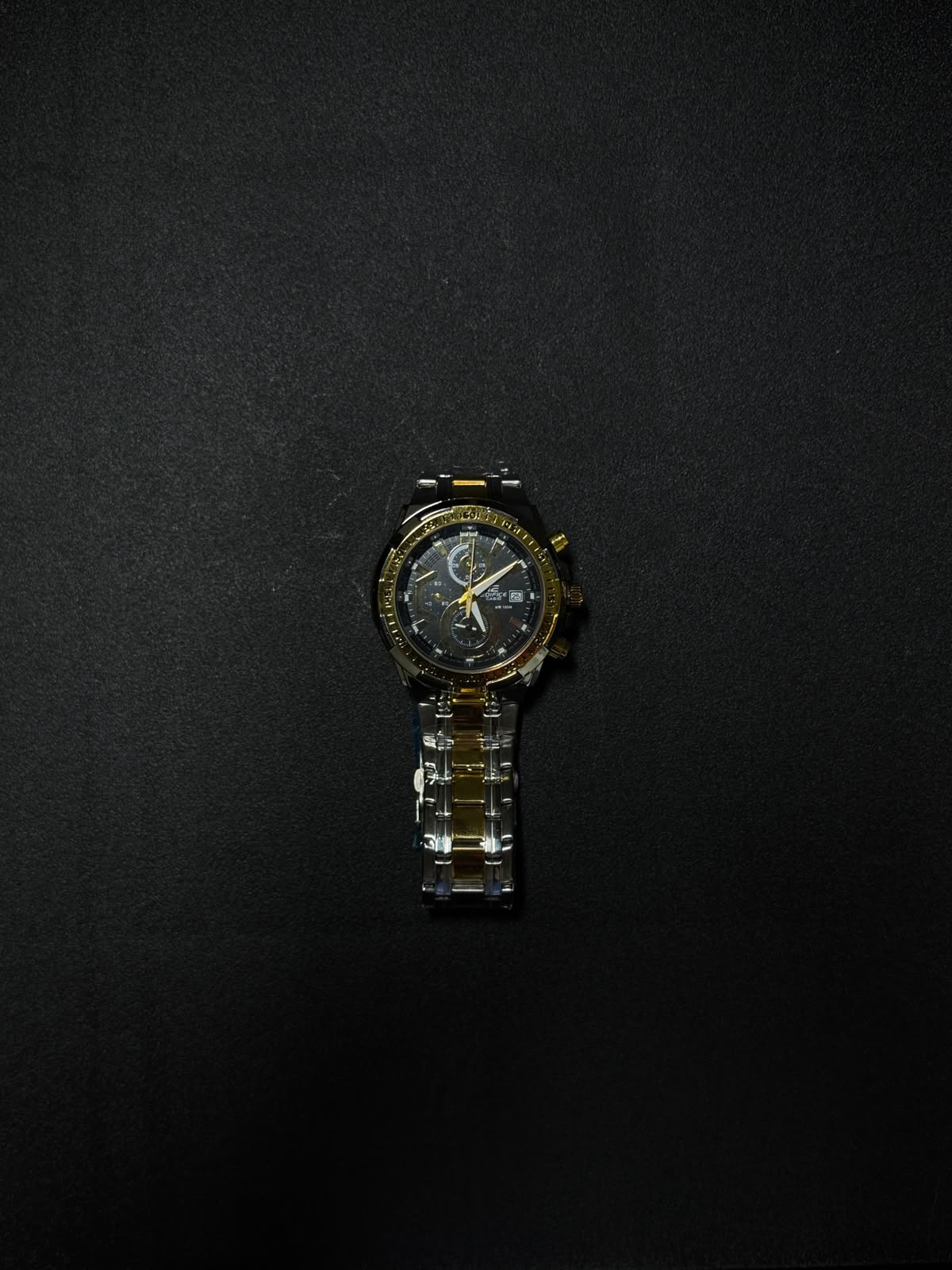 Black and gold replica men's watch featuring a chronograph-style dial, metal bracelet and premium luxury design on black background.