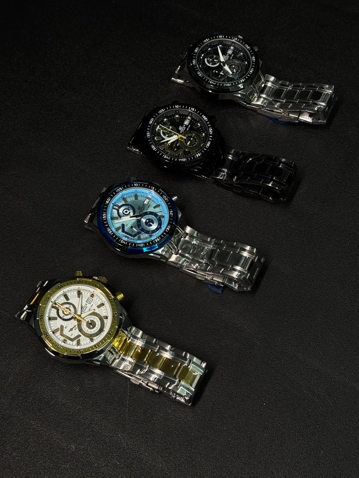 Premium replica chronograph watch collection featuring black, blue, gold-white and green dial variants with stainless steel bracelets on a dark textured background.