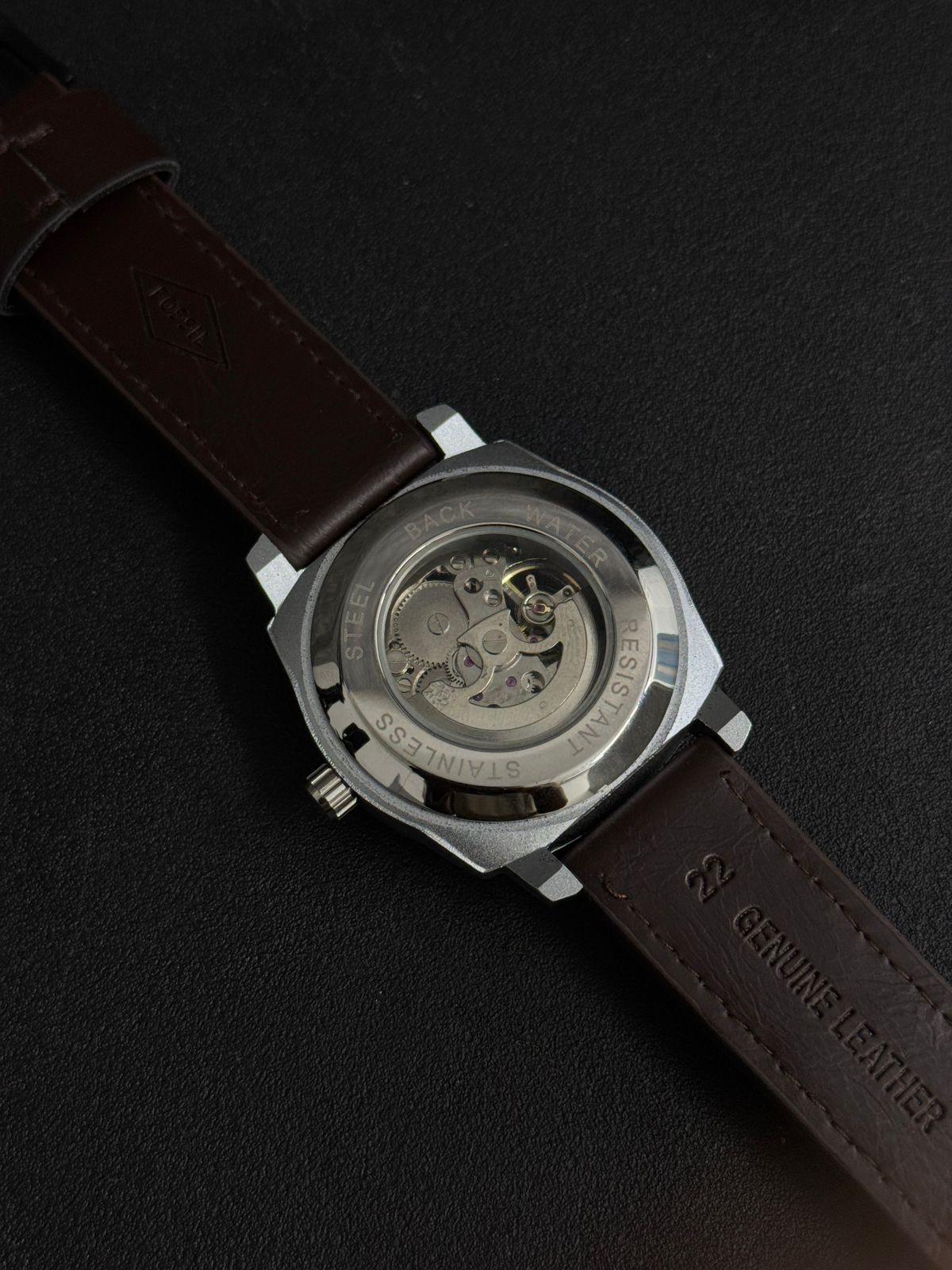 Automatic-style replica watch back view featuring transparent exhibition case back and brown leather strap on black background
